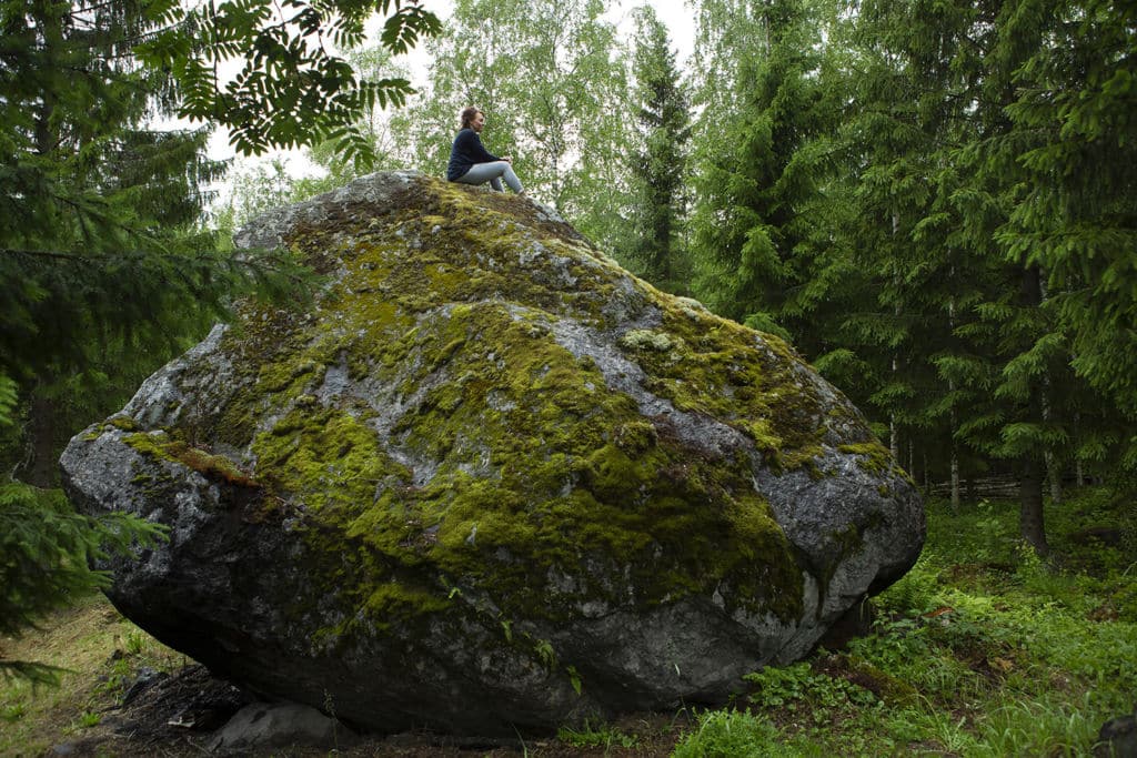 Mari Tuhkanen istuu suuren kiven päällä