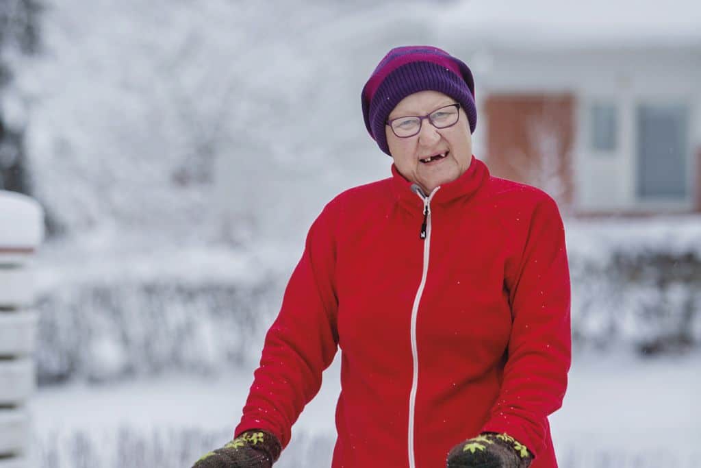 Ikääntynyt nainen lenkillä rollaattorin kanssa lumisessa maisemassa.