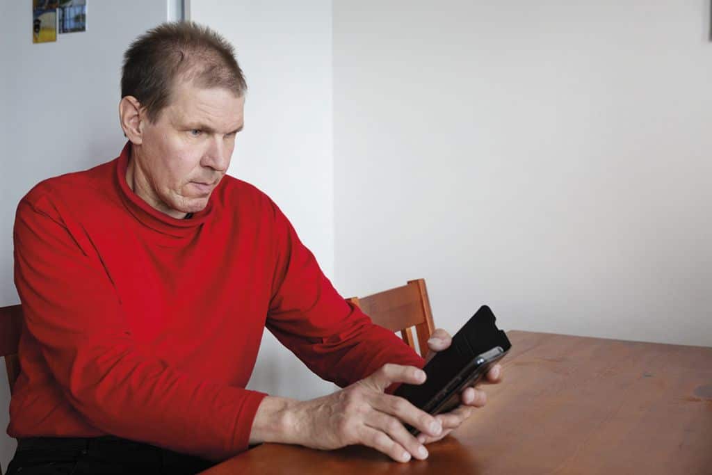 Mies käyttää älypuhelinta kotonaan pöydän äänerrä.
