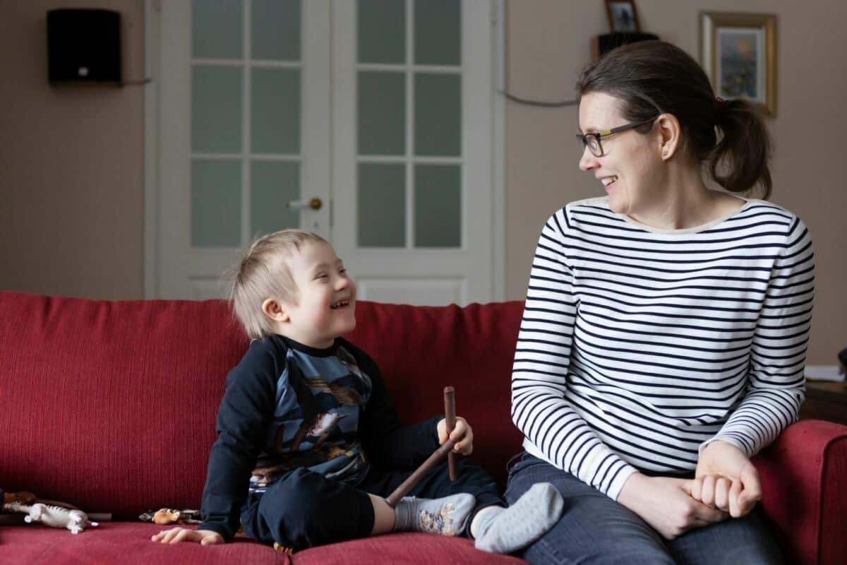 Mervi Talvitie ja Leo-poika katsovat toisiaan hymyillen olohuoneessa punaisella sohvalla.