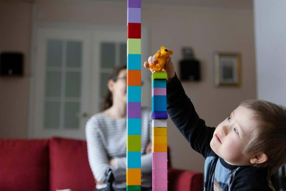 Leo Mälkiä kokoaa tornia palikoista olohuoneessa. Mervi-äiti istuu takana sohvalla.