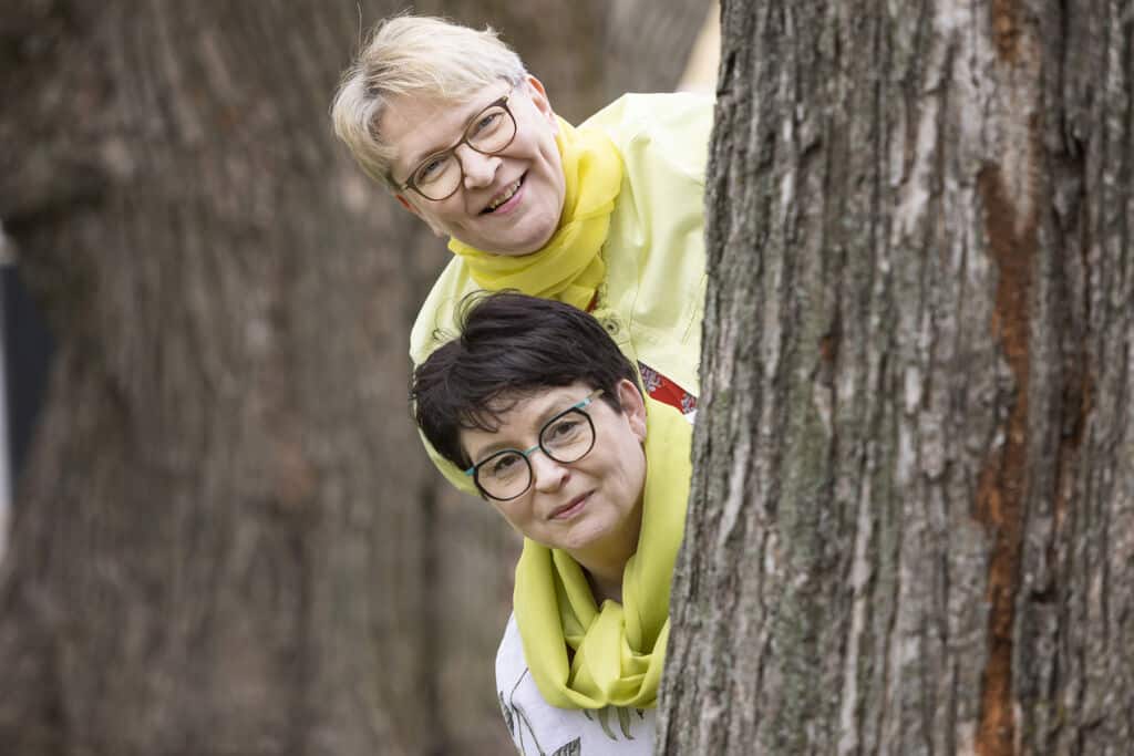 Kaksi naista kurkistaa puun takaa