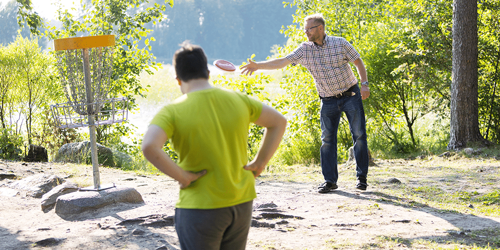 Sijaisisä Petri Hartikainen heittää frisbeetä ja sijaispoika katselee kuvan etualalla.