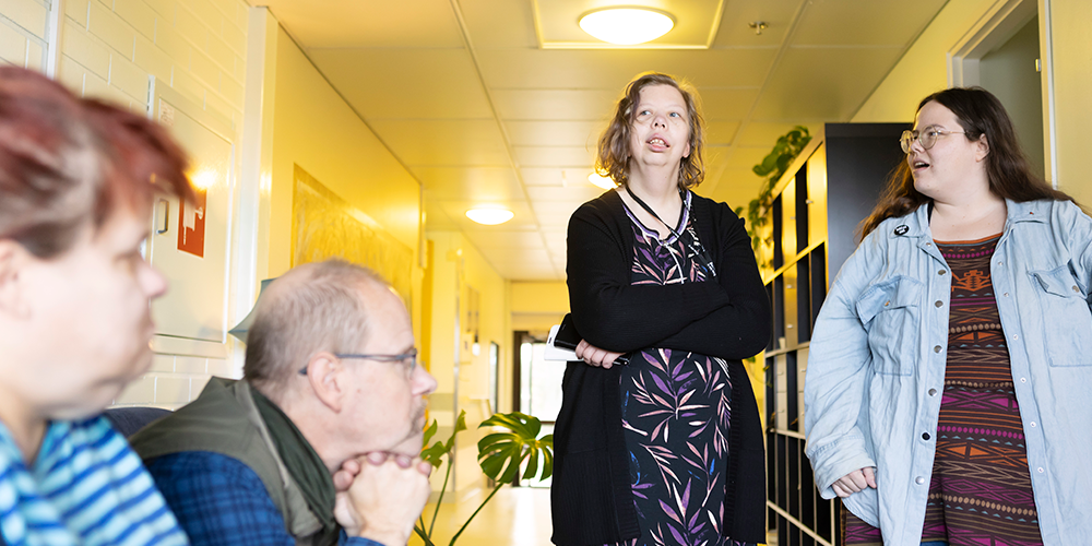 Anna Valkama kertoo avustajansa Viljatuuli Ylikosken kanssa asumiseen liittyvistä kokemuksistaan toimintakeskus Resiinassa. Toimintakeskuksen kävijät istuvat kuuntelemassa.