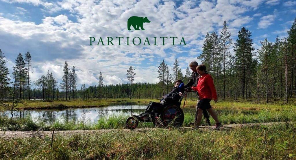 Partioaitan karhu-logo . Logon alla luontomaisema, jossa mies ja nainen vaeltavat työntäen maastorattaissa istuvaa nuorta. Yhdenvertaisesti luontoon -retkellä Pudasjärvellä.