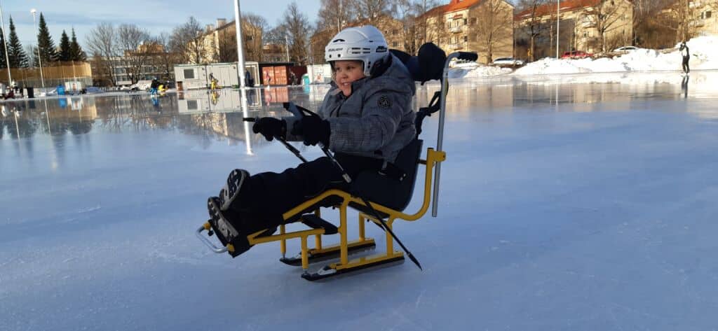 Lapsi istuu luistelukelkassa ja työntää sauvoilla vauhtia.