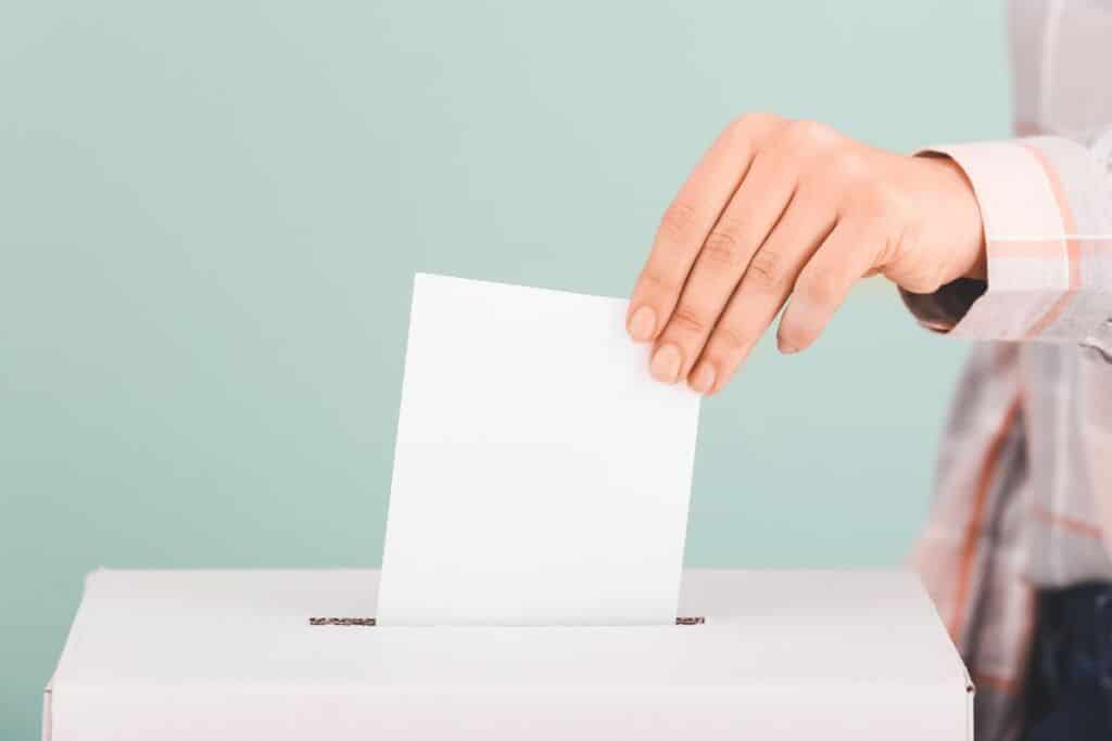Käsi laittaa äänestyslippua äänestyslaatikkoon.