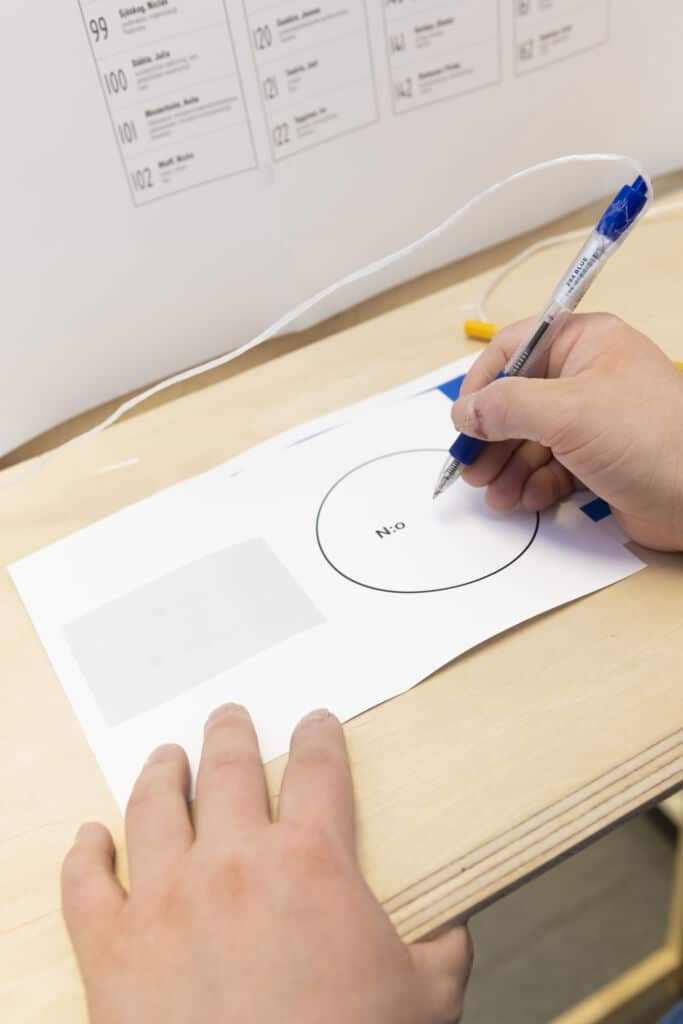 Pöydällä on äänestyslipuke, johon ihminen on alkamassa kirjoittaa valitsemaansa numeroa.