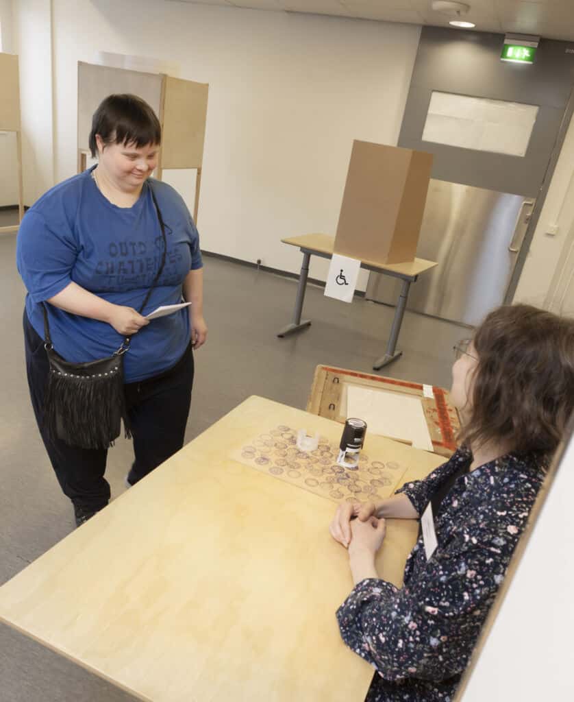 Nainen tuo vaalivirkailijalle äänestyslipuketta.